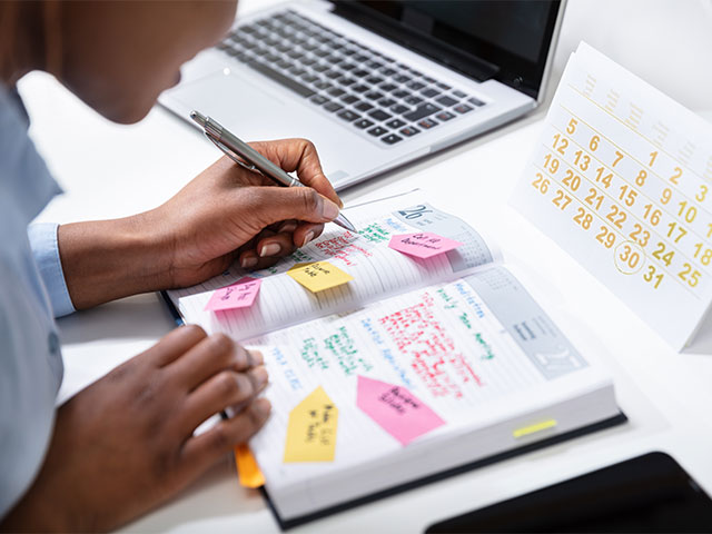 A woman diligently writes in a notebook, surrounded by colorful sticky notes for organization and reminders.