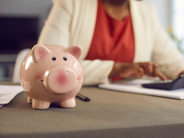 A female professional diligently working at a desk, with a pink ceramic smiling piggy bank placed in front of her.