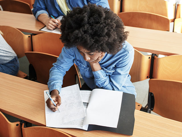 A female student seated at a desk in a classroom, engaged in learning and taking notes.