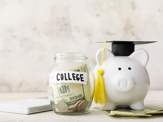 a glass savings jar filled with money, labeled "college", next to a ceramic piggy bank wearing a black graduation cap with a yellow tassel