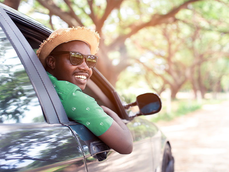 Student smiling out passenger window in car driving off campus