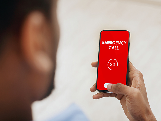 Emergency Planning View over shoulder of man holding phone with 24 hour support line on red screen