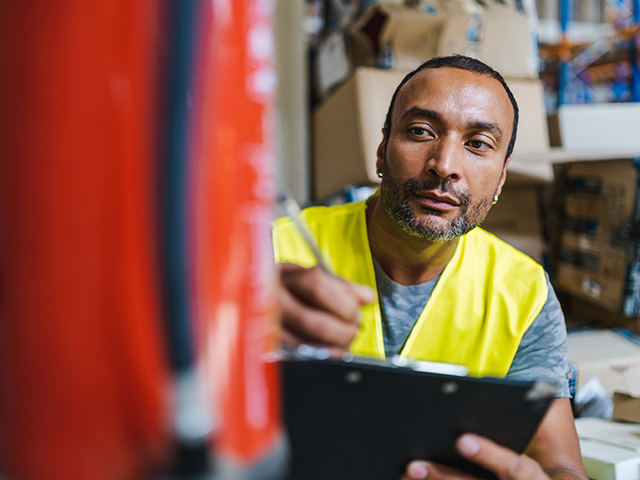 Fire Safety african american worker with pen and clipboard checking and inspecting a fire extinguisher