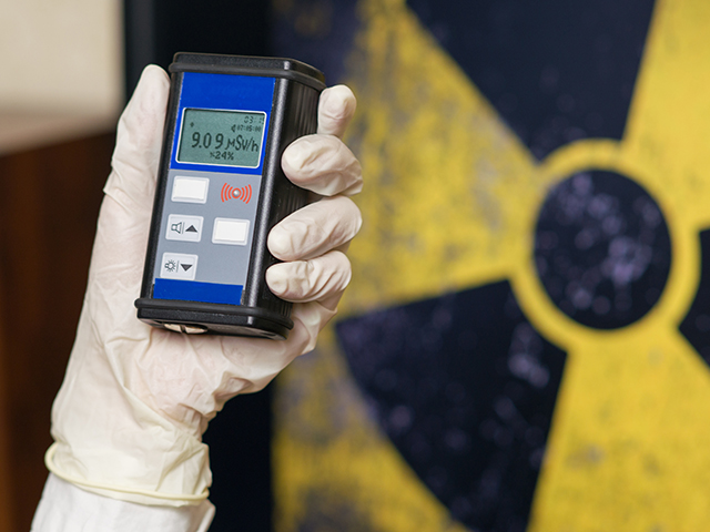 Radiation Safety Management Person wearing white gloves holding a Geiger counter with radioactive materials in the background