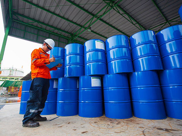 Regulated Fuel Storage Compliance A male inspection worker holding a pen and clipboard, looking at a stock of oil drum barrels