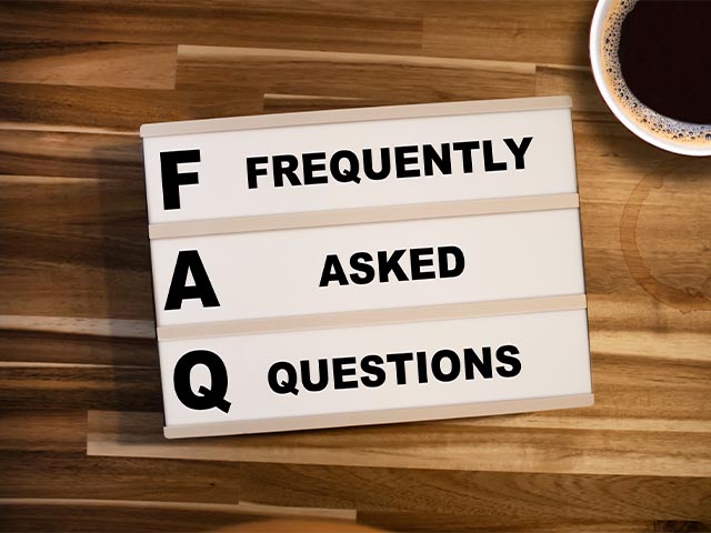 the words "frequently asked questions" on a sign sitting on a wooden desk with a cup of coffee