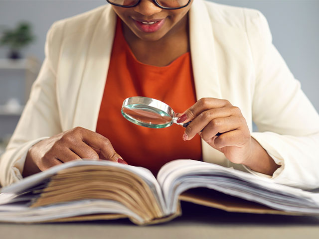 Woman looking at book with magnifying glass