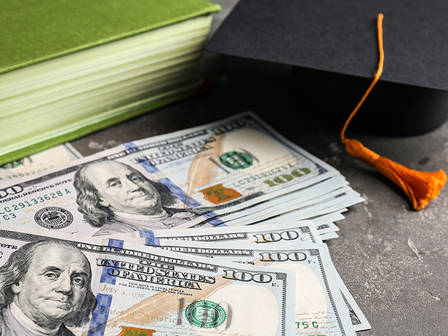 grad cap sitting next to a green book and a spread of money