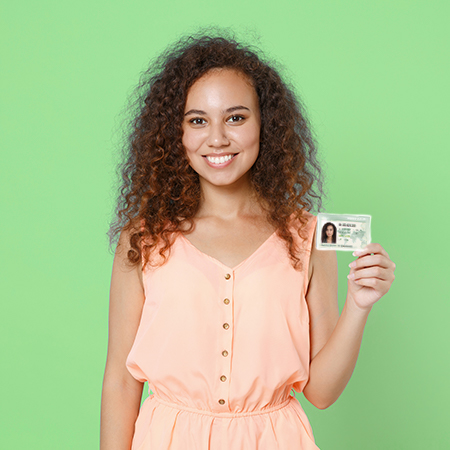 Smiling young African American woman holding Passport Card infront of green background