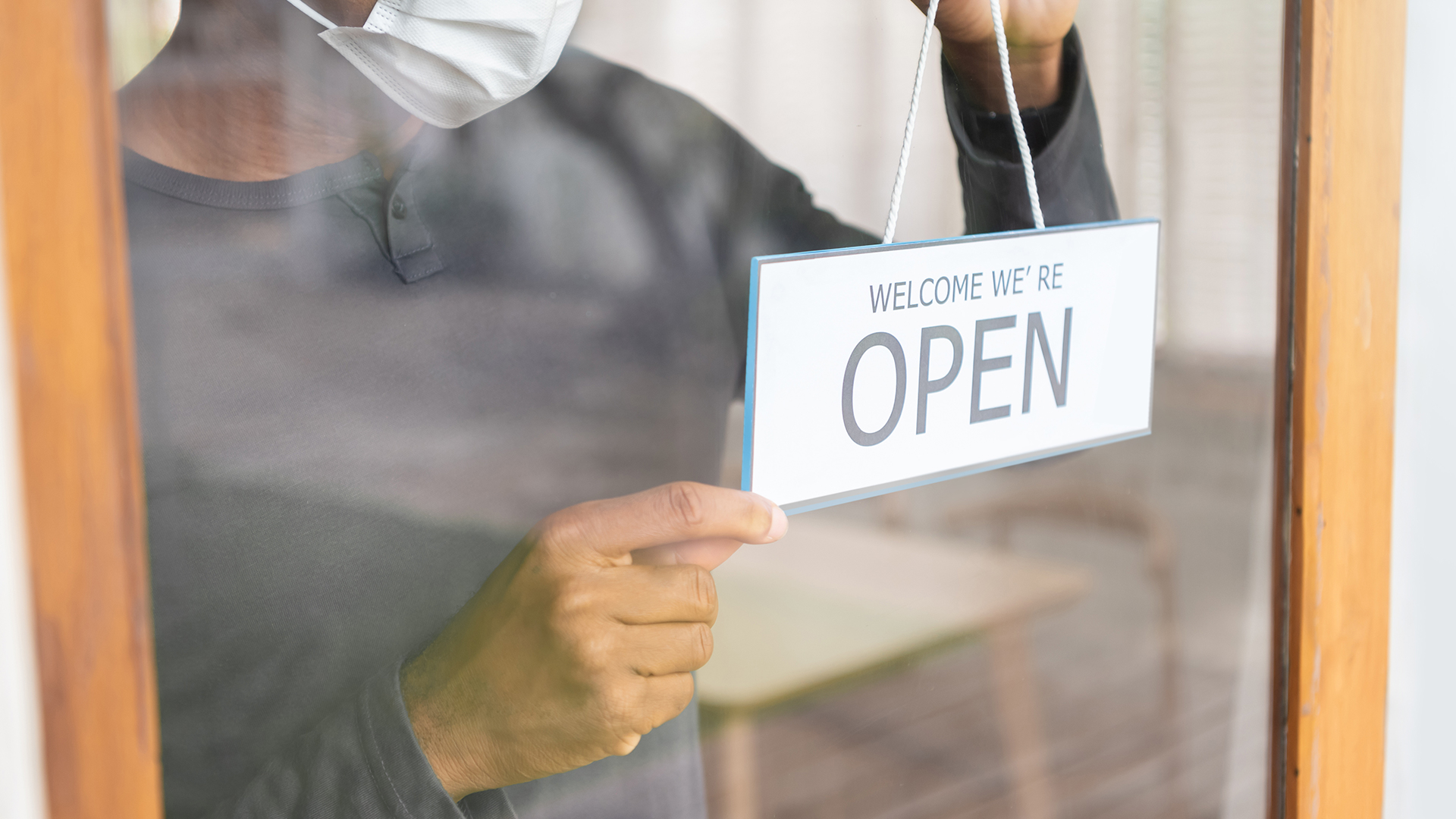 Man hanging up a "Welcome we're open" sign on a glass door