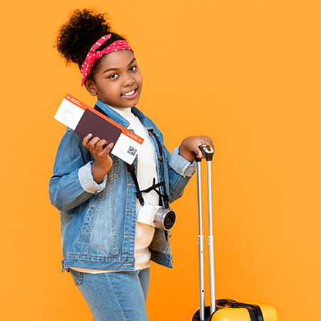 Smiling traveling African American little girl wih baggage, passport, and boarding pass, infront of orange background
