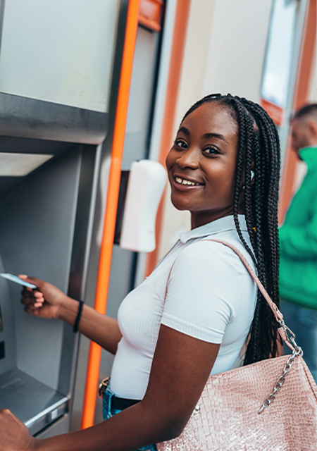 Why is Financial Literacy so Important? young woman using an ATM, smiling at the camera