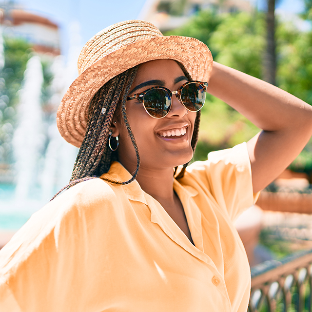 A young woman smiling and wearing a straw hat and sunglasses