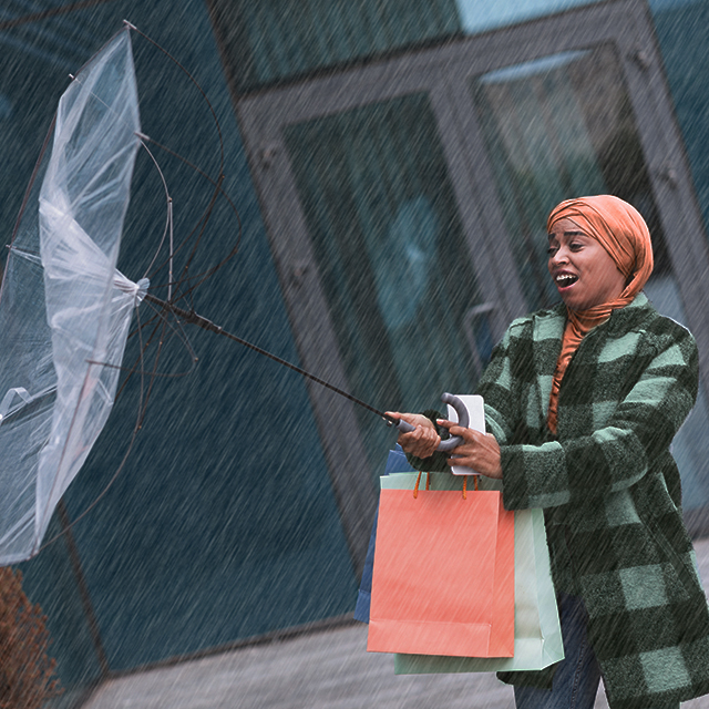 Young woman with a surprised expression caught in windy and rainy weather, her umbrella turned inside out because of the weather